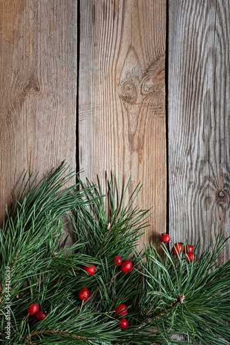 Branches of a Christmas tree (pine) with rose hips on a wooden background. Christmas and New Year, Winter holidays concept. Top view and copy space.