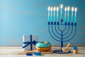 Jewish holiday Hanukkah concept with menorah, traditional donuts and gift box on wooden table.