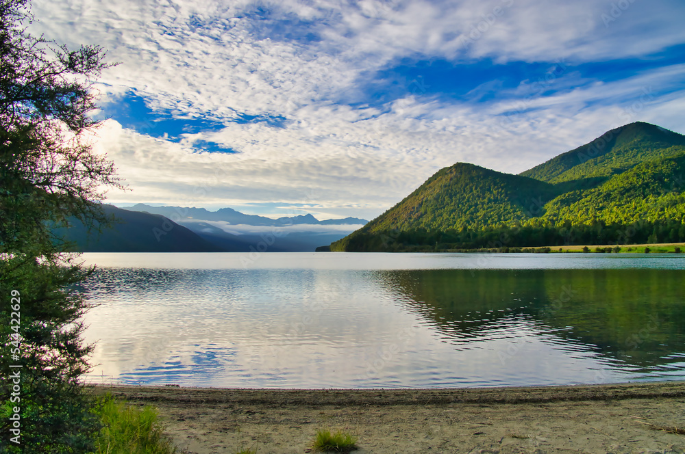 Naklejka premium Lake Rotoroa, Nelson Lakes National Park, New Zealand, on an early summer morning, with the low sun illuminating the green mountains and mist hanging in the valley 