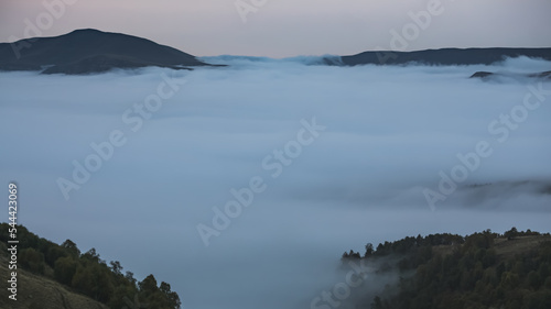 Low clouds in the mountains filled the entire valley and mountain peaks and hills stick out above the clouds  on an autumn twilight evening