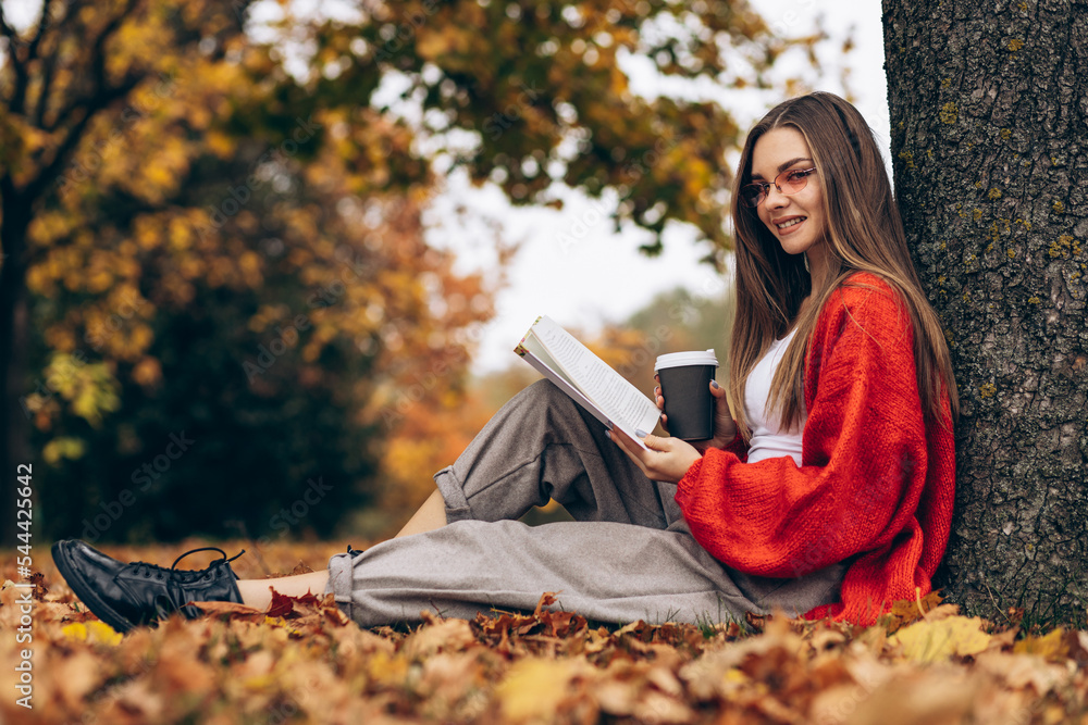 Woman reading in an autumn park and drinking coffee under the tree Woman reading in an autumn park and drinking coffee under the tree