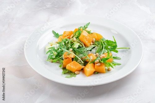 Italian vegetarian salad of baked pumpkin with pine nuts, arugula and cheese. Bright fresh salad with pumpkin slices
