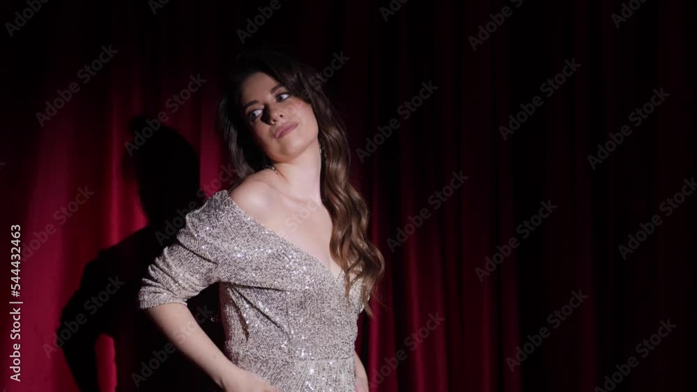 beautiful young woman in a shiny dress posing in front of the camera near red gift boxes with bows in a spot of light beautiful young woman in a shiny dress posing in front of the camera near red gift boxes with bows in a spot of light