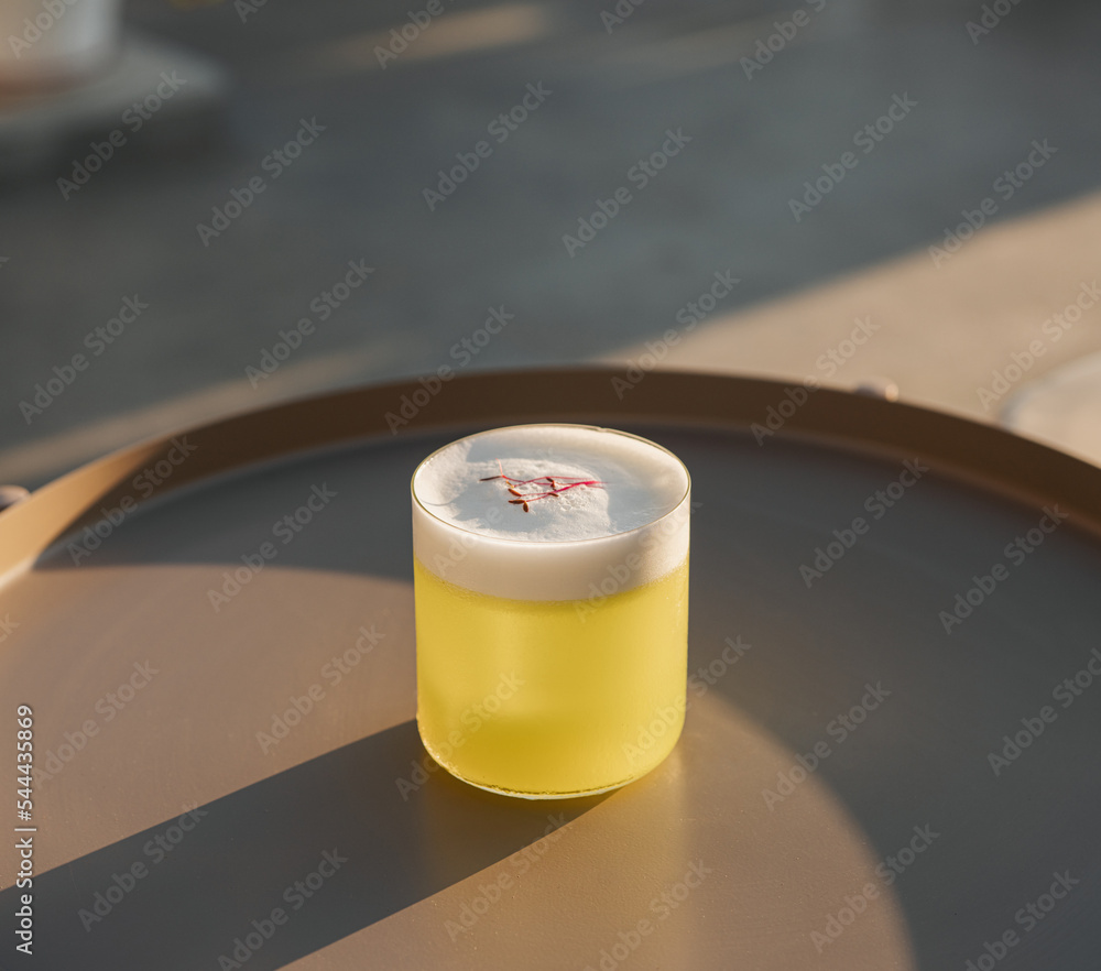 Elegant stemware glass of fresh orange cocktail with big ice ball on white table surface, bright yellow background. Spring summer art drink food concept Elegant stemware glass of fresh orange cocktail with big ice ball on white table surface, bright yellow background. Spring summer art drink food concept