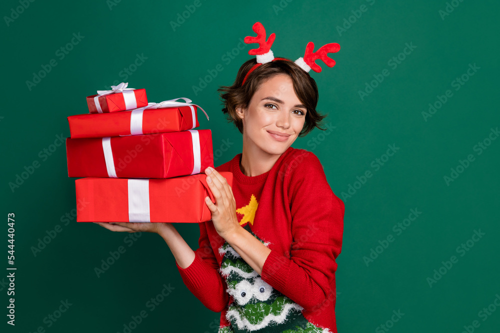 Photo of adorable pretty girl dressed ugly print pullover deer hair band holding bow packages pile isolated green color background Photo of adorable pretty girl dressed ugly print pullover deer hair band holding bow packages pile isolated green color background