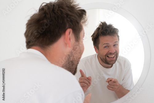 Man trying to encourage himself showing thumb up looking in mirror. 