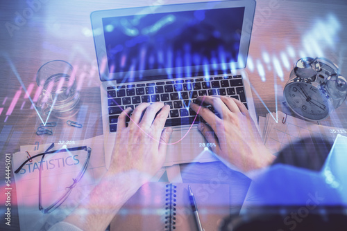 Double exposure of man's hands typing over laptop keyboard and forex chart hologram drawing. Top view. Financial markets concept.