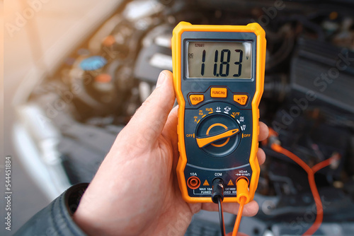 Man testing car electrical system including battery, alternator for winter. Check car battery using voltmeter. Man use multimeter with voltage range measurement to check up voltage level. Low voltage photo