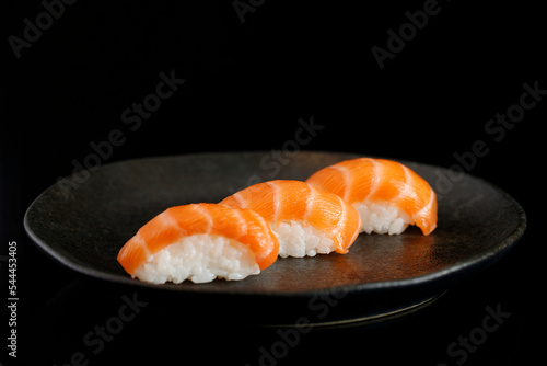 Gray plate with 3 pieces of raw salmon rice sushi on a black background