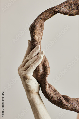 Fototapeta Close up of hand covered in plaster holding ceramic art piece minimal