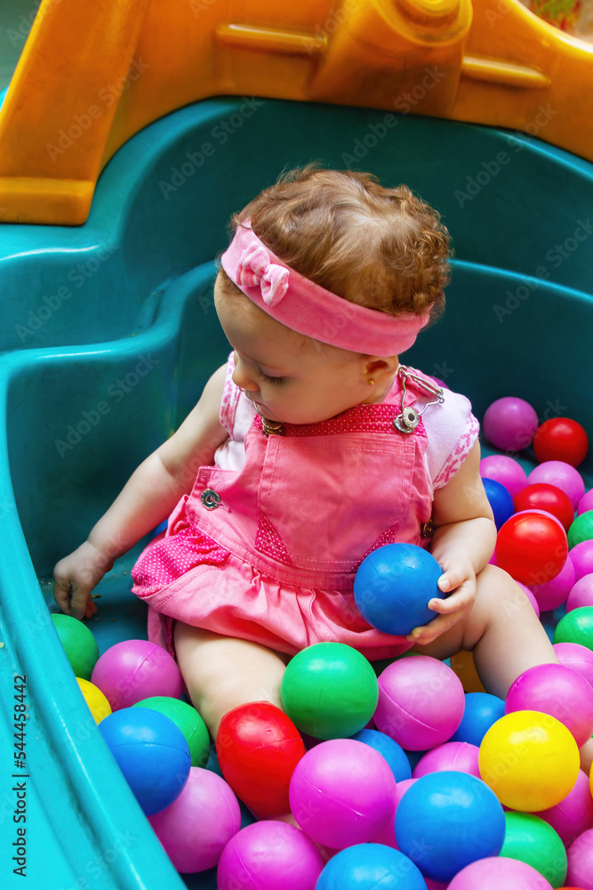 Obraz premium Baby girl playing in colorful polka dot pool in ball bath