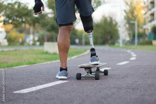 Close-up of person with disability on skateboard. Man with mechanical leg skateboarding in park on sunny day. Sport, disability concept