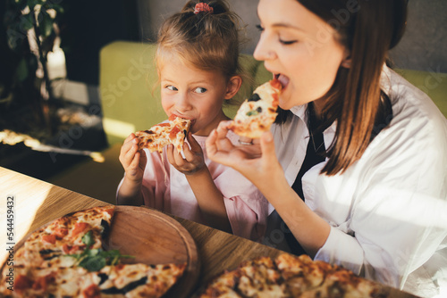 Mother and daughter eat pizza in a cafe.