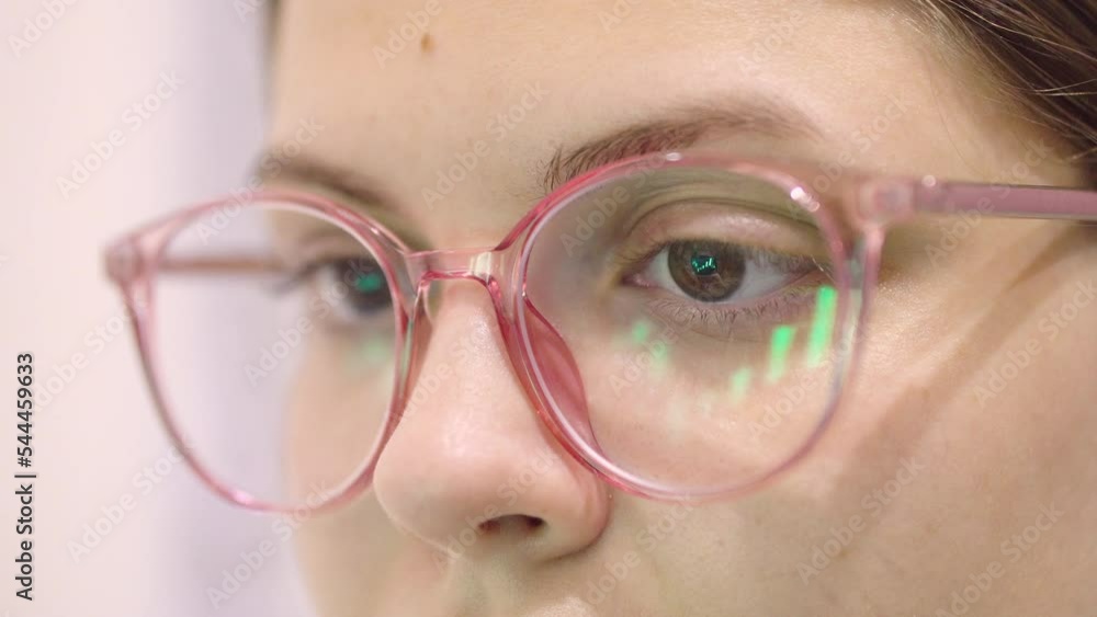 Closeup - female eyes in eyeglasses scrolling in front of laptop. The reflection of the laptop screen on the glasses Closeup - female eyes in eyeglasses scrolling in front of laptop. The reflection of the laptop screen on the glasses
