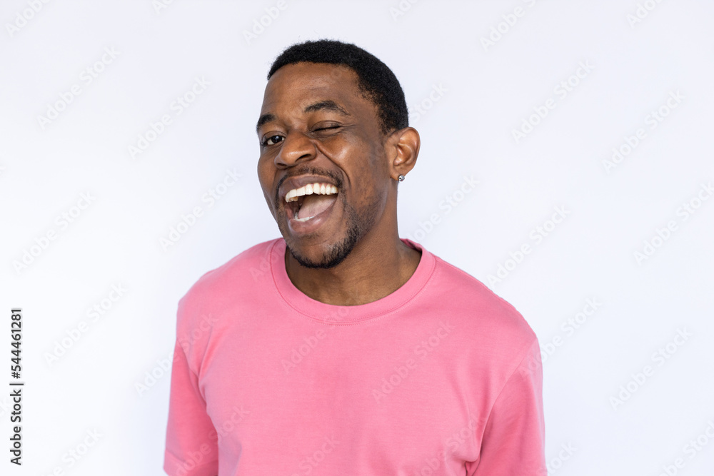 Portrait of playful African American man winking. Happy young male model with short dark hair in pink T-shirt looking at camera with open mouth, smiling with wink. Success, flirt concept Portrait of playful African American man winking. Happy young male model with short dark hair in pink T-shirt looking at camera with open mouth, smiling with wink. Success, flirt concept
