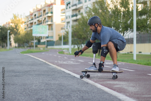 Calm man with mechanical leg in casual clothes skateboarding. Mid adult sportsman riding down special road in concentration, doing tricks. Sport, disability, training concept