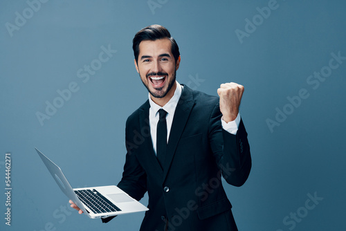 Man business stares at laptop and works online via internet in business suit video call happy smile with teeth fist bump happiness on blue background copy place