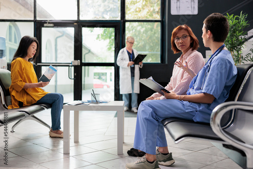 Medical nurse taking notes on papers at examination with old asian patient, doing checkup visit in hopsital waiting room. Assistant writing report at appointment with woman. Medicine support photo