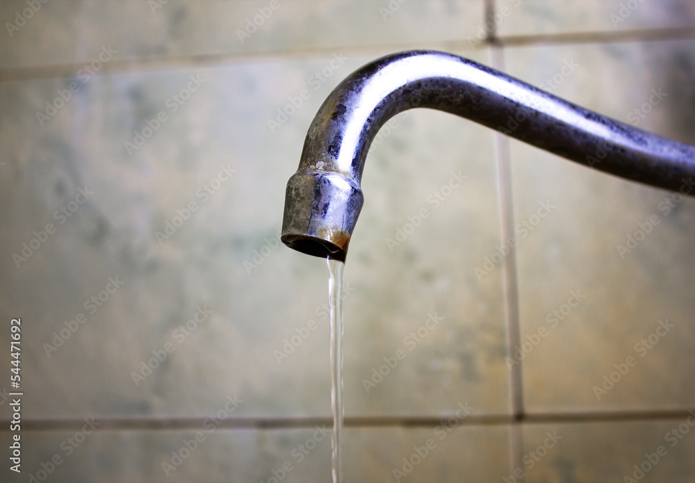 A thin stream from an old faucet in the bathroom. An old water faucet. A thin stream from an old faucet in the bathroom. An old water faucet.