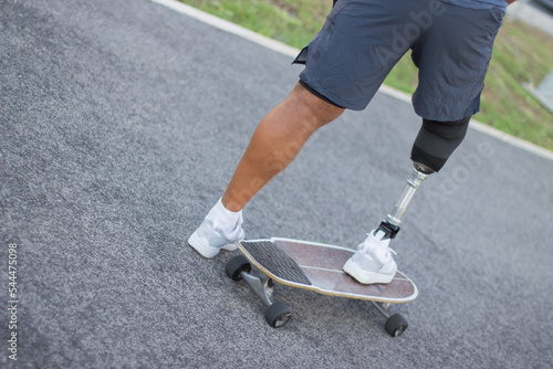 Close-up of sportsman with disability in park on sunny day. Man in casual clothes and sportive protection riding skateboard. Sport, disability, training concept