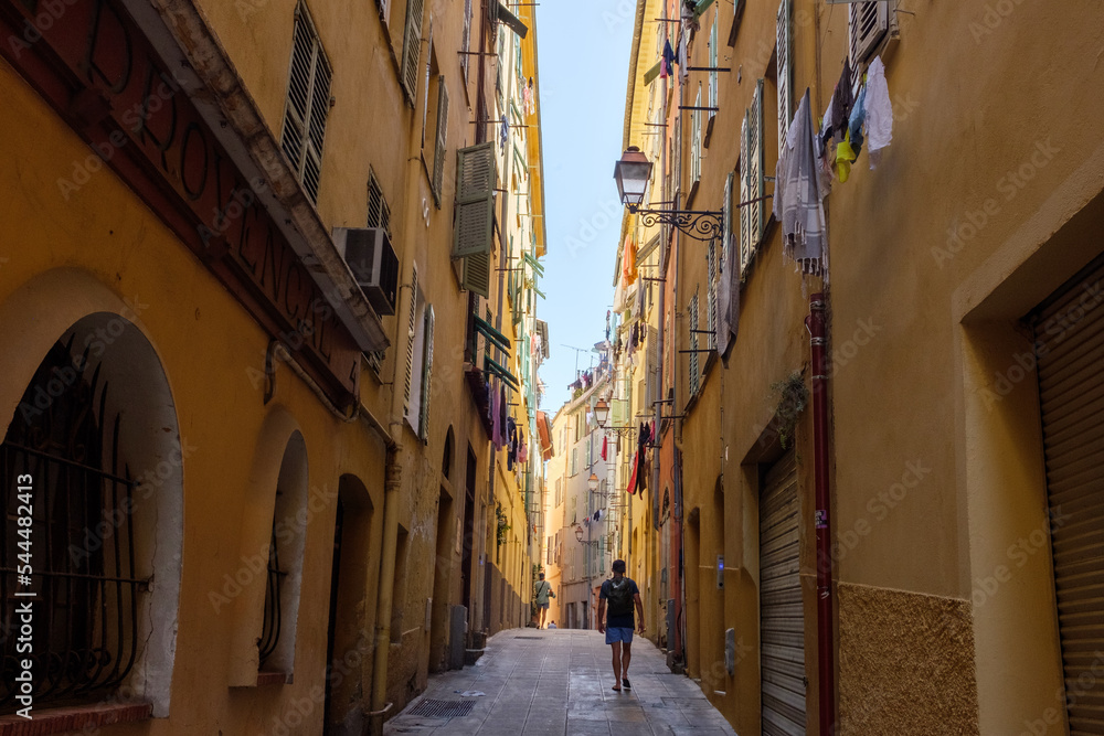 People walk down a narrow street in the old city of Nice, France