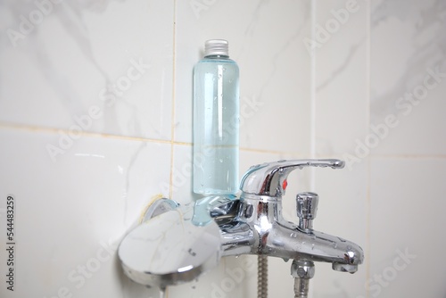 Bottle of shower gel on faucet in bathroom. Space for text