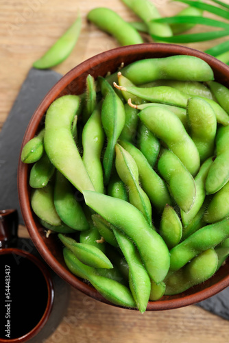 Green edamame beans in pods served with soy sauce on wooden table, flat lay