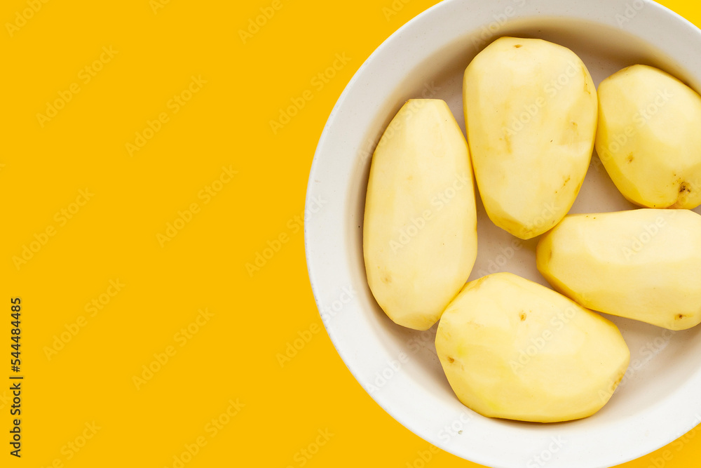 Raw peeled potatoes in bowl on yellow background. Raw peeled potatoes in bowl on yellow background.