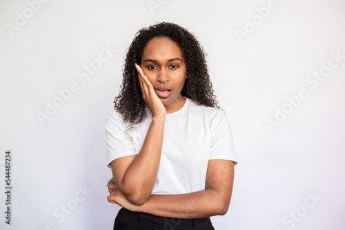 Portrait of distrustful young woman looking at camera. African American lady wearing white T-shirt standing with bored expression over white background. Boredom and distrust concept © KAMPUS