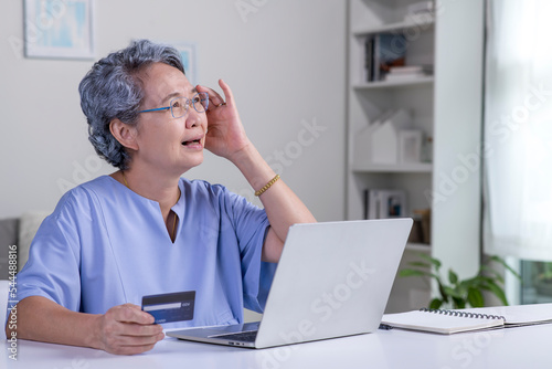 Confused Asian elderly senior retired woman, stressed worried sad frustrated female having problem with paying, buying online, payments with credit blocked bank card, laptop. Internet fraud