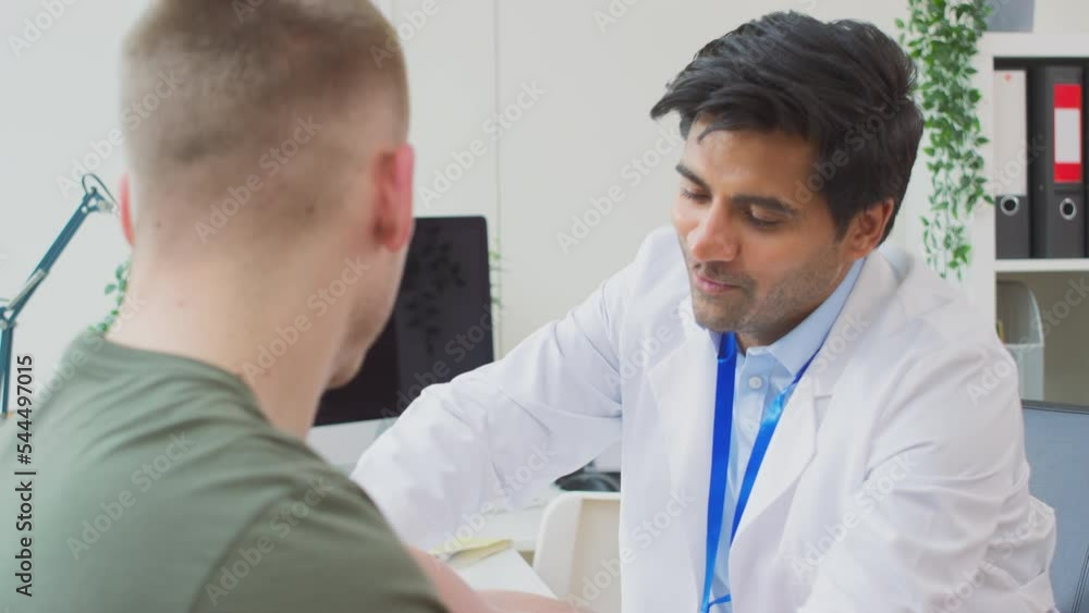 Male doctor or GP wearing white coat examining young man taking blood pressure with sphygmomanometer - shot in slow motion Male doctor or GP wearing white coat examining young man taking blood pressure with sphygmomanometer - shot in slow motion