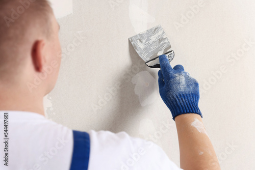 Man plastering wall with putty knife indoors, closeup. Home renovation
