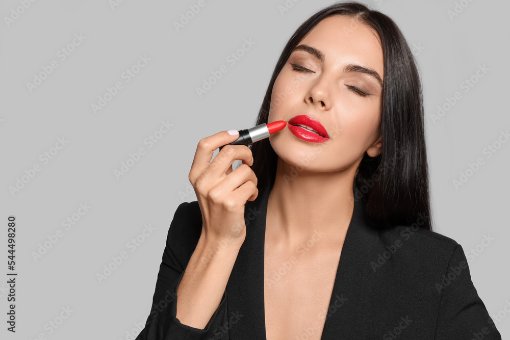 Young woman with beautiful makeup holding red lipstick on light gray background. Space for text Young woman with beautiful makeup holding red lipstick on light gray background. Space for text