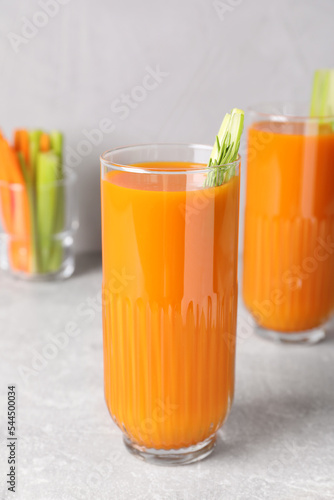 Glasses of tasty carrot juice with celery sticks on light grey table