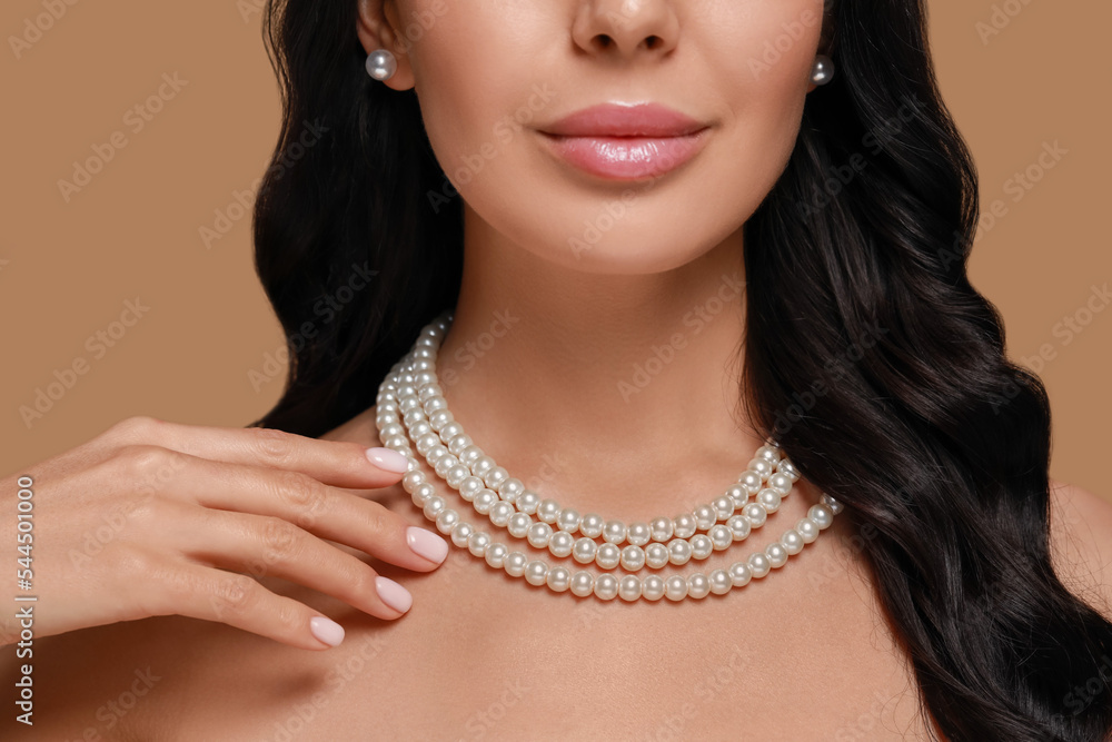 Young woman wearing elegant pearl jewelry on brown background, closeup