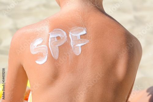 Child with abbreviation SPF of sunscreen on back at beach, closeup