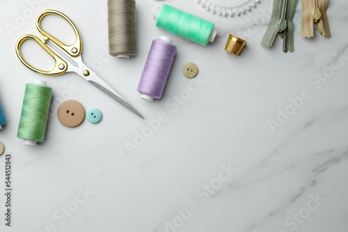 Threads and other sewing supplies on white marble table, flat lay. Space for text © New Africa
