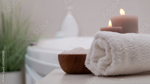 Rolled bath towel, sea salt and burning candles on table in bathroom, closeup. Space for text