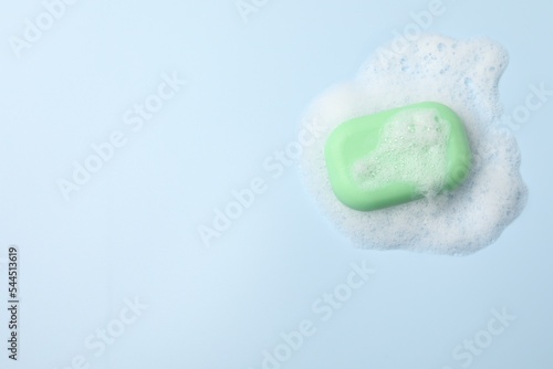 Soap and fluffy foam on light blue background, top view. Space for text