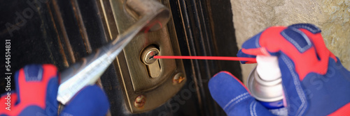 Fényképezés Handyman in gloves pouring penetrating lubricant into door lock closeup