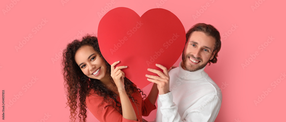 Happy young couple with red paper heart on pink background. Valentine's Day celebration Happy young couple with red paper heart on pink background. Valentine's Day celebration