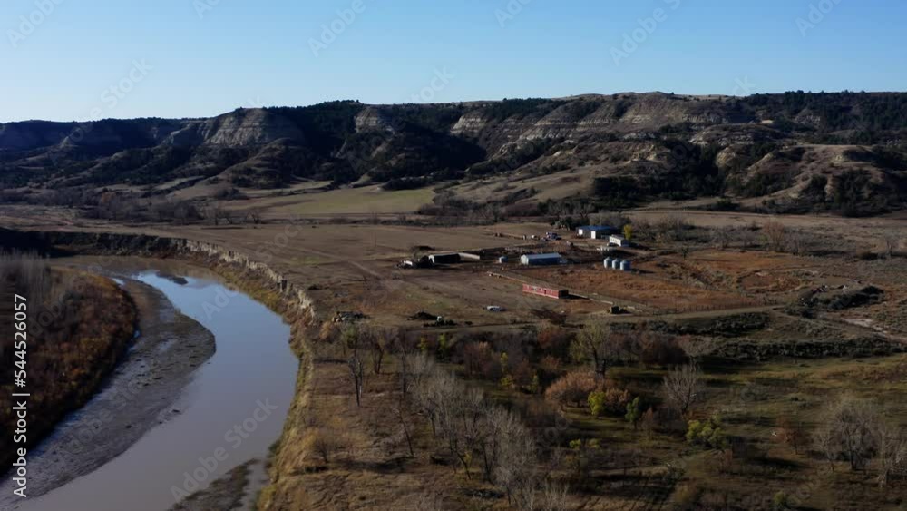 Aerial Fly Over River Establishing View of Rural Farm Ranch in Vast Wild Prairie, Dry Arid Land Terrain Around the Ranch and Mountain in Horizon, Grassy Butte North Dakota Landscape Aerial Fly Over River Establishing View of Rural Farm Ranch in Vast Wild Prairie, Dry Arid Land Terrain Around the Ranch and Mountain in Horizon, Grassy Butte North Dakota Landscape