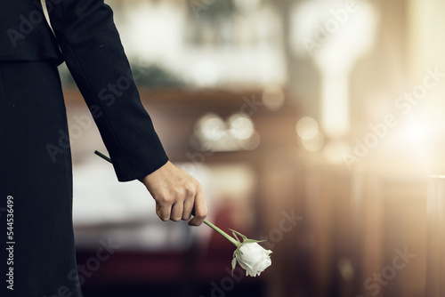 Flower, funeral and hand holding rose in mourning at death ceremony with grief for loss burial. Floral, church or cemetary with person holding plant for sad bereavement or cemetary event in a chapel photo