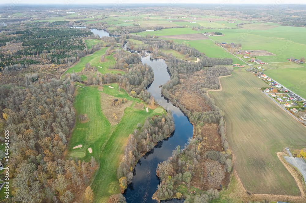 Aerial panoramic view of beautiful autumn nature, golf course, river, multicolored trees and green grass, warm sunlight
