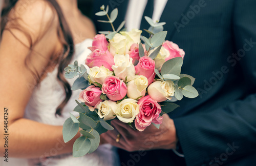 Flowers, wedding and love with a bouquet in the hands of a bride and groom on their marriage day closeup. Rose, married and celebration event with a floral arrangement in hand during a ceremony