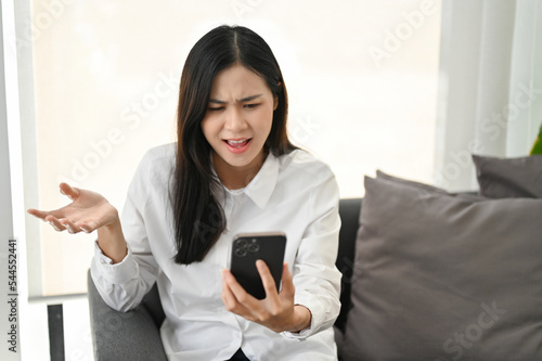 Foto Unhappy and dissatisfied Asian woman sitting on sofa, receiving unreasonable new