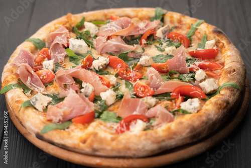 Pizza with prosciutto, arugula and parmesan on wooden background, top view. Italian cuisine.