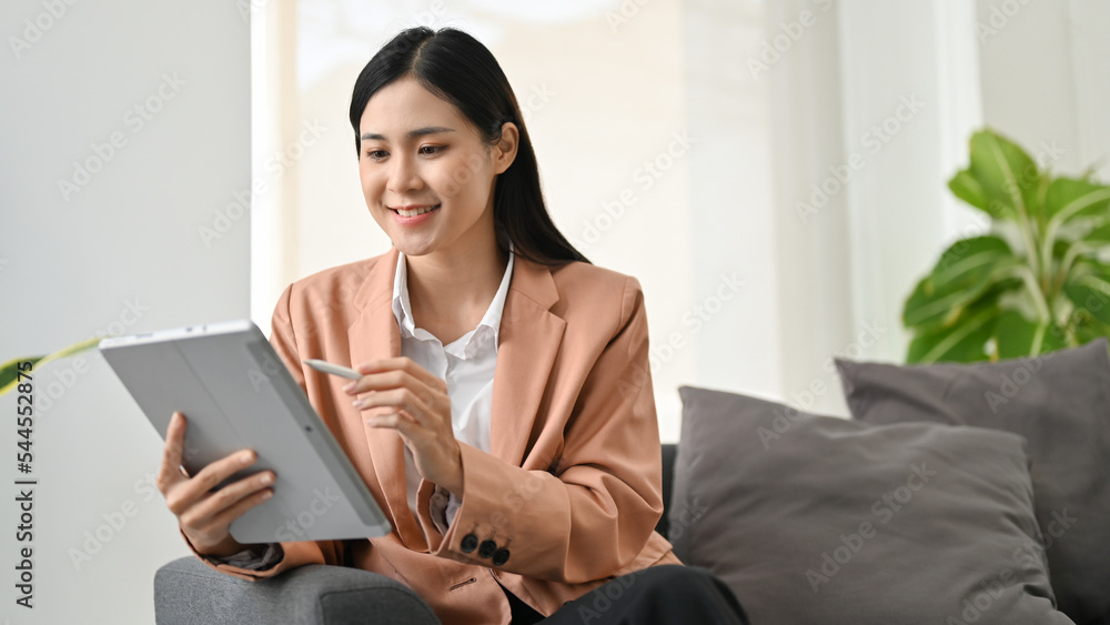 Attractive Asian businesswoman sitting on sofa, using her portable digital tablet. Attractive Asian businesswoman sitting on sofa, using her portable digital tablet.