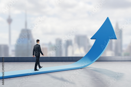 Obraz na płótnie Young businessman walking on abstract upward blue arrow on blurry city background