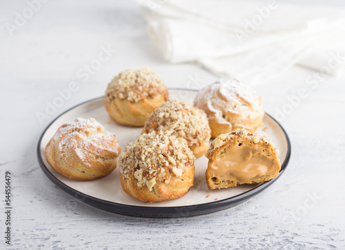 Gluten-free oat profiteroles with caramel cream of boiled condensed milk, sprinkled with powdered sugar and nuts on a light blue background. Delicious homemade food photo